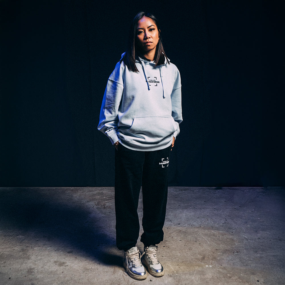 Femme habillée avec le Jogging Basics 2.0 noir et un hoodie assorti, coupe unisexe et confortable, design épuré