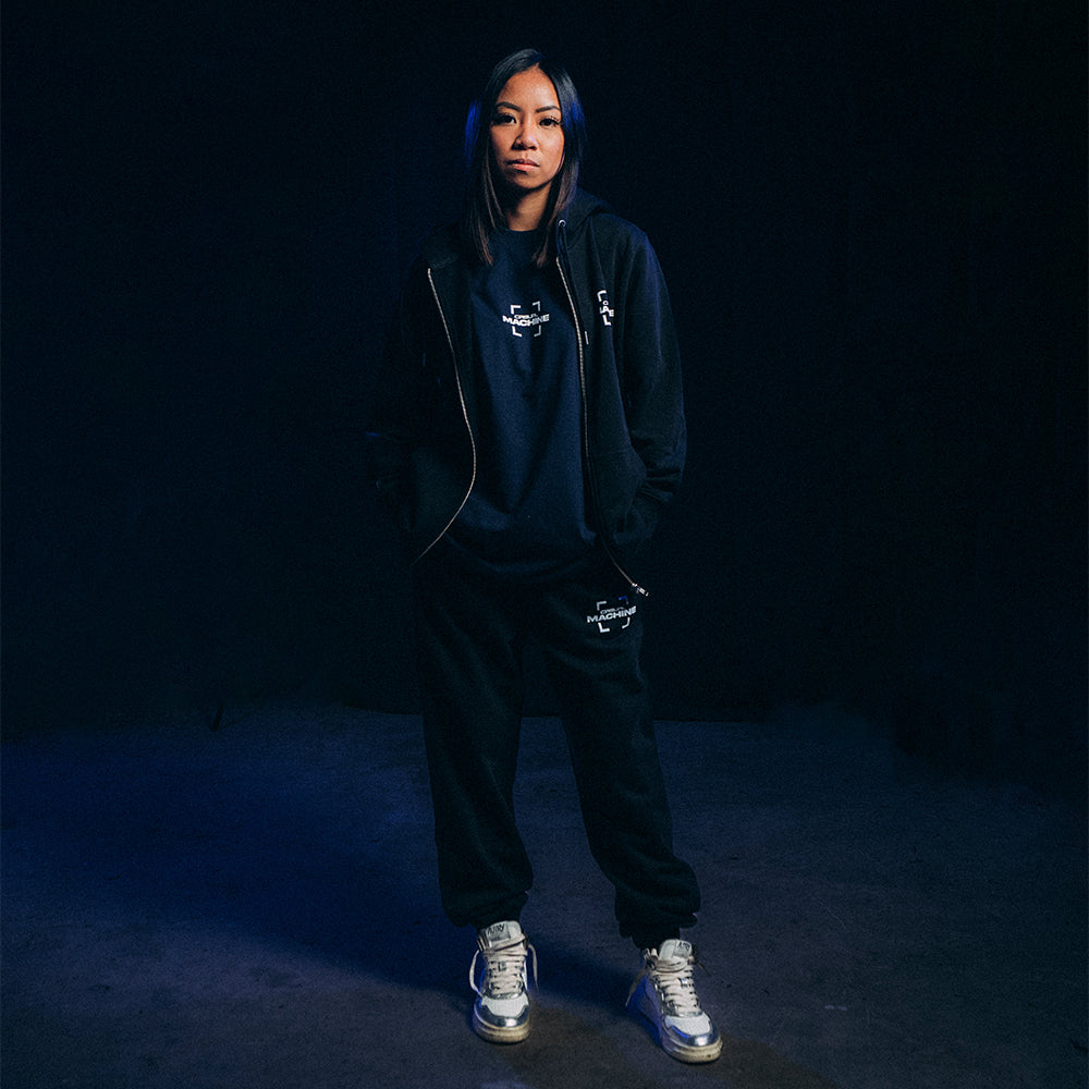 Femme portant le Jogging Basics 2.0 noir avec une veste assortie, coupe unisexe, coton organique 400 g, style casual minimaliste